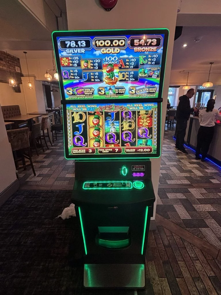 Neon-lit slot machine with green trim in a lounge, top payout readouts show Silver/Gold/Bronze amounts and colorful reels below.